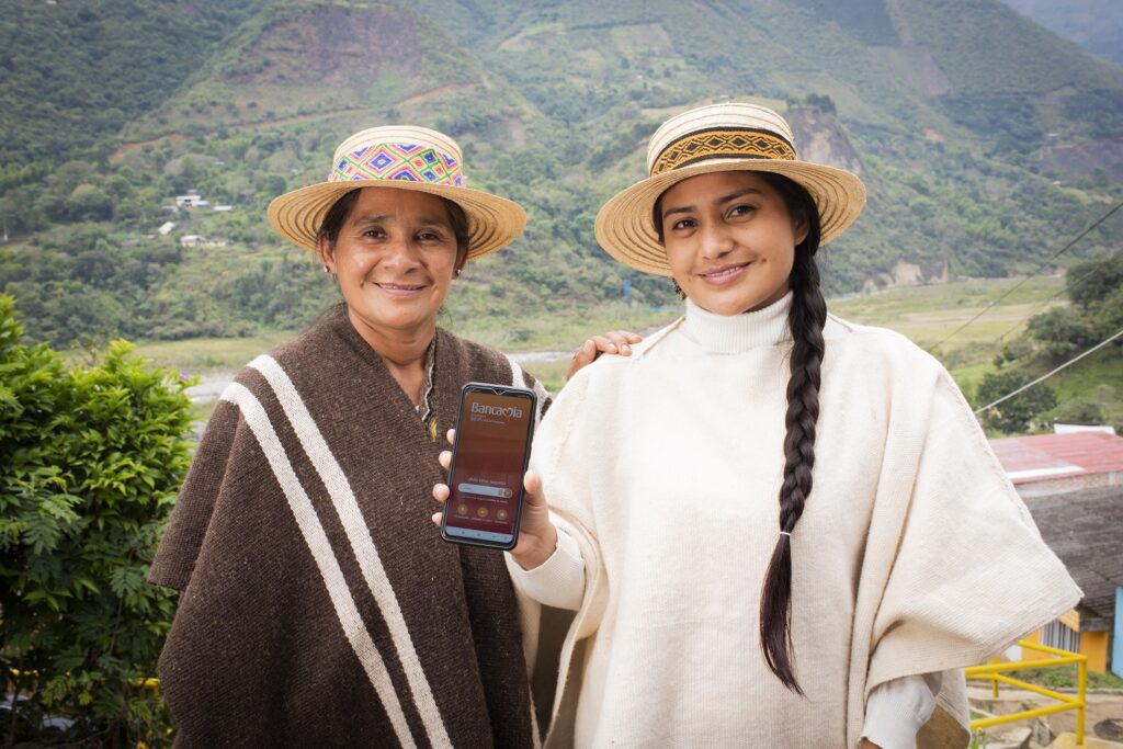 La emprendedora colombiana de Bancamía (FMBBVA) Florinda Chavez, que confecciona sombreros de manera artesanal, y su hija, que trabaja en el negocio, junto al asesor que les explica el funcionamiento de la app de banca móvi
