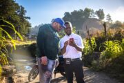 Rumaldo Álvarez, in his farm, with a Banco Adopem microcredit analyst who teaches him how to use mobile banking