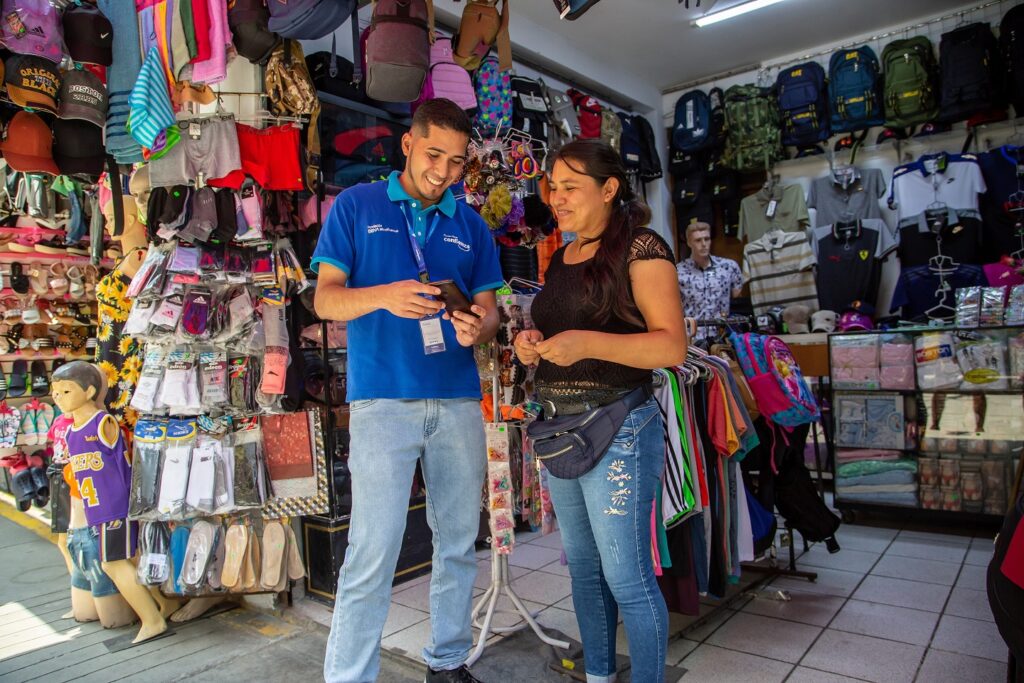 José Romero visita el puesto de venta de una emprendedora y le explica el funcionamiento de la banca móvil (Financiera Confianza, FMBBVA)